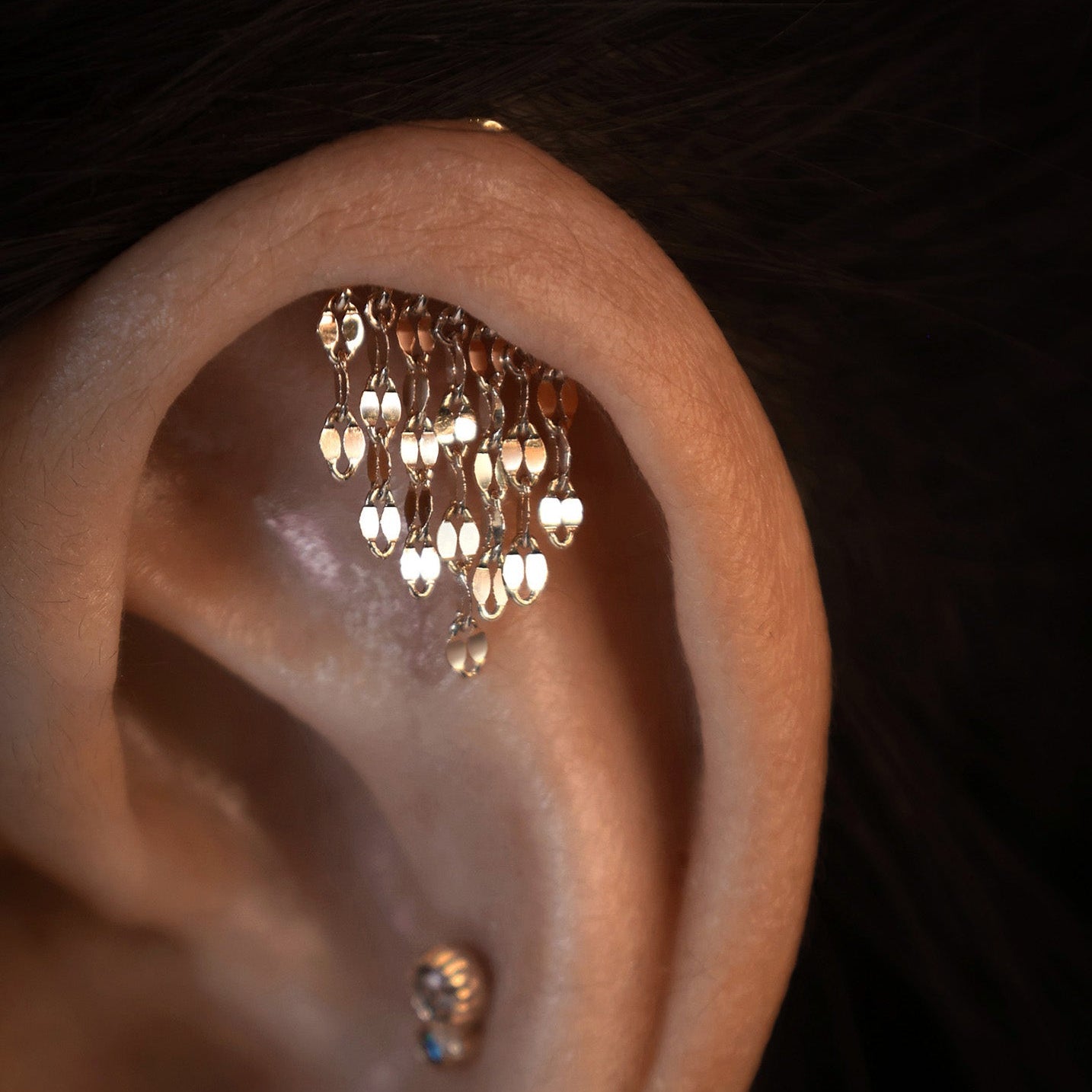 Close-up of an ear with a gold earring featuring dangling drops.