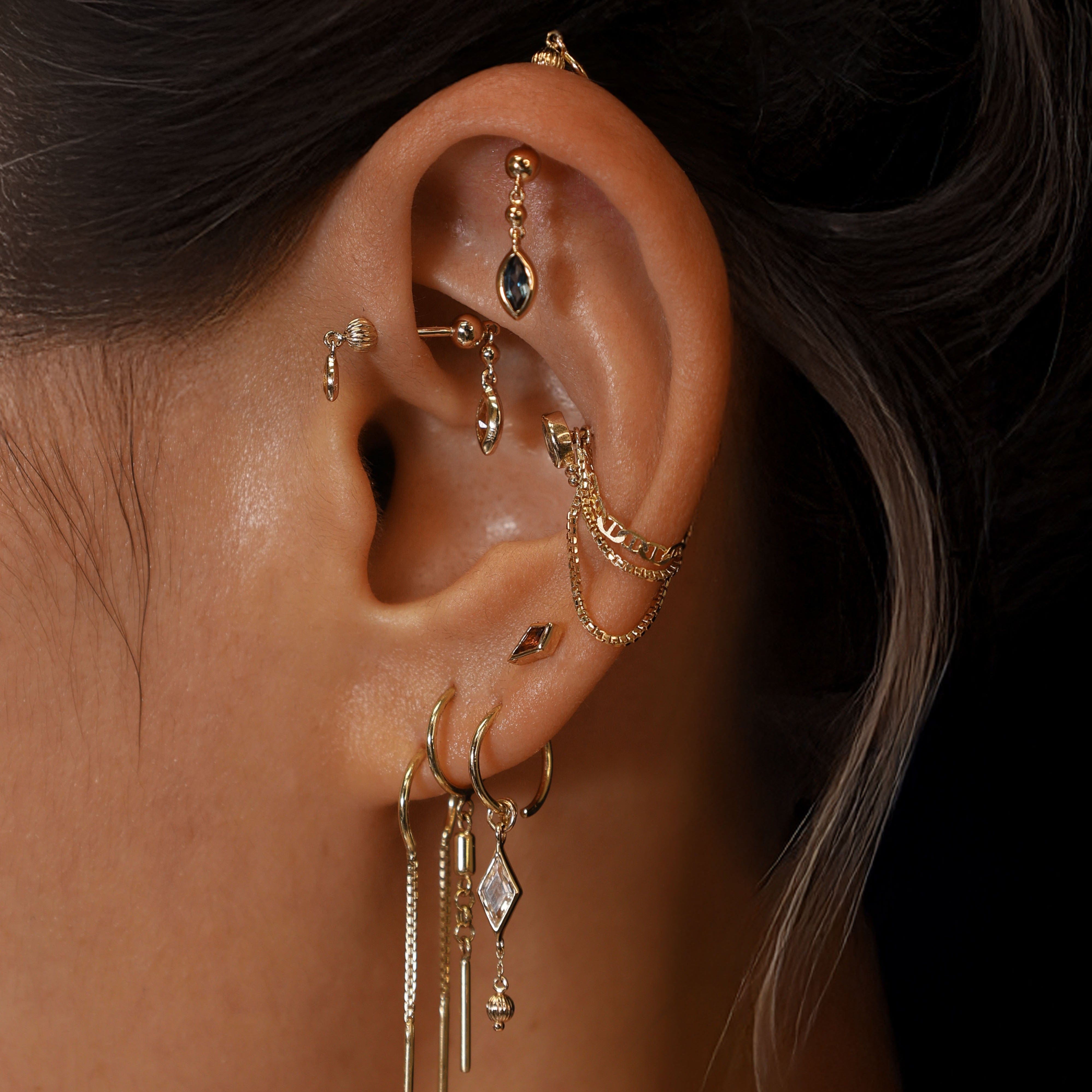 Close-up of an ear with multiple gold earrings against a dark background