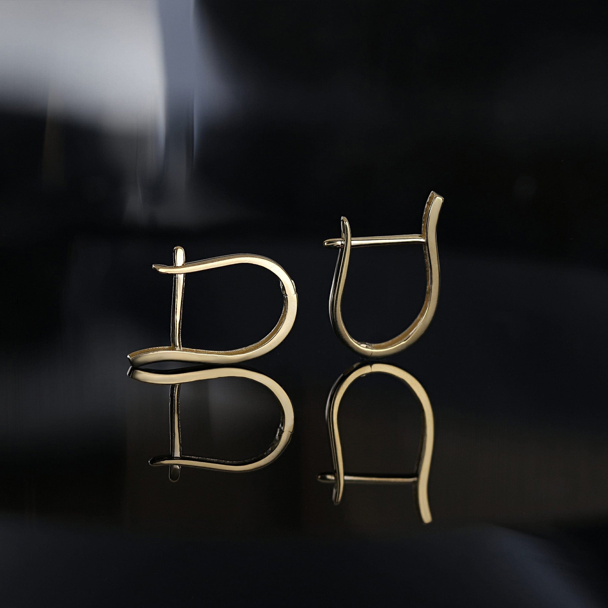 Pair of gold earrings on a reflective black surface with a dark background