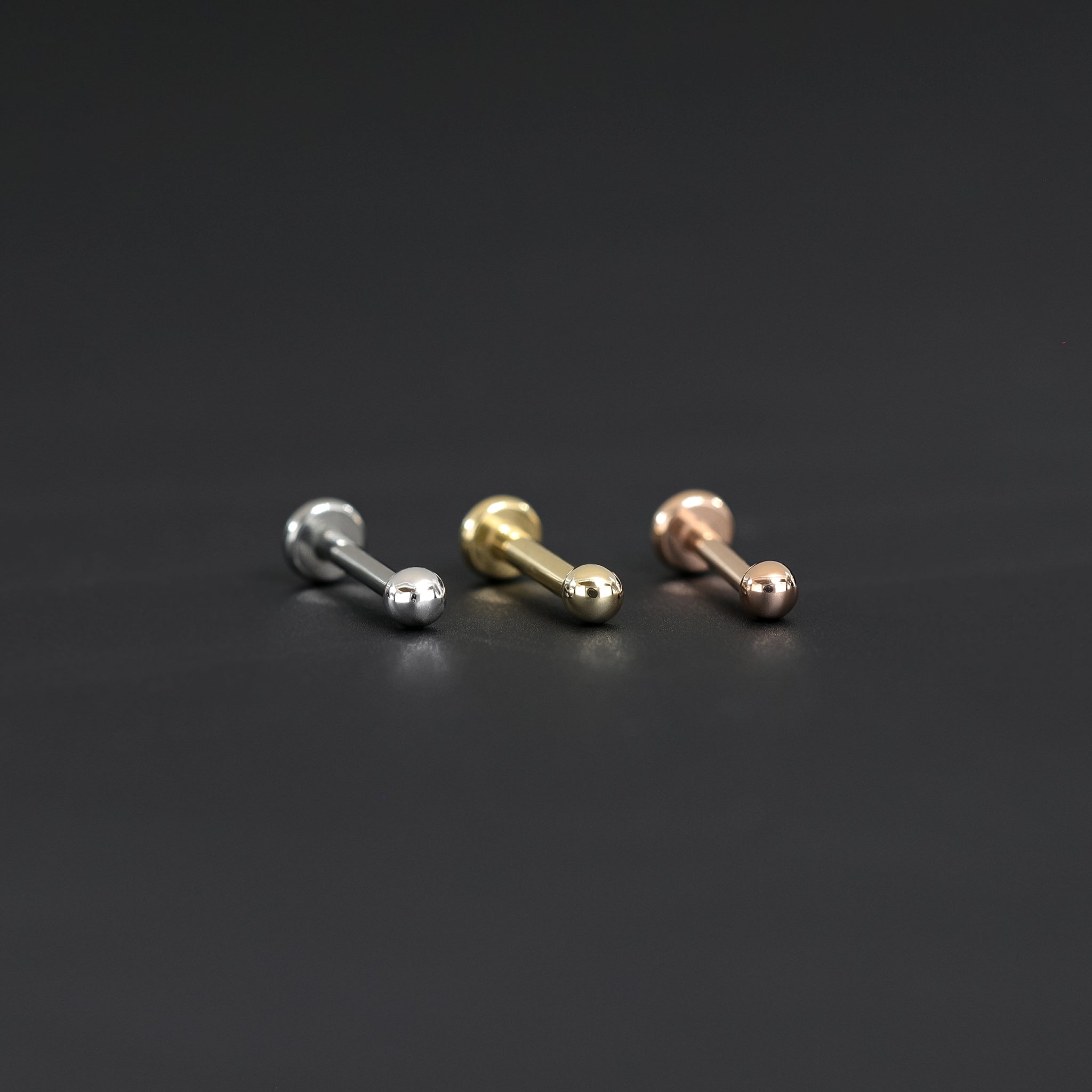 14K Gold Ball studs in yellow gold, white gold and rose gold displayed on black surface.