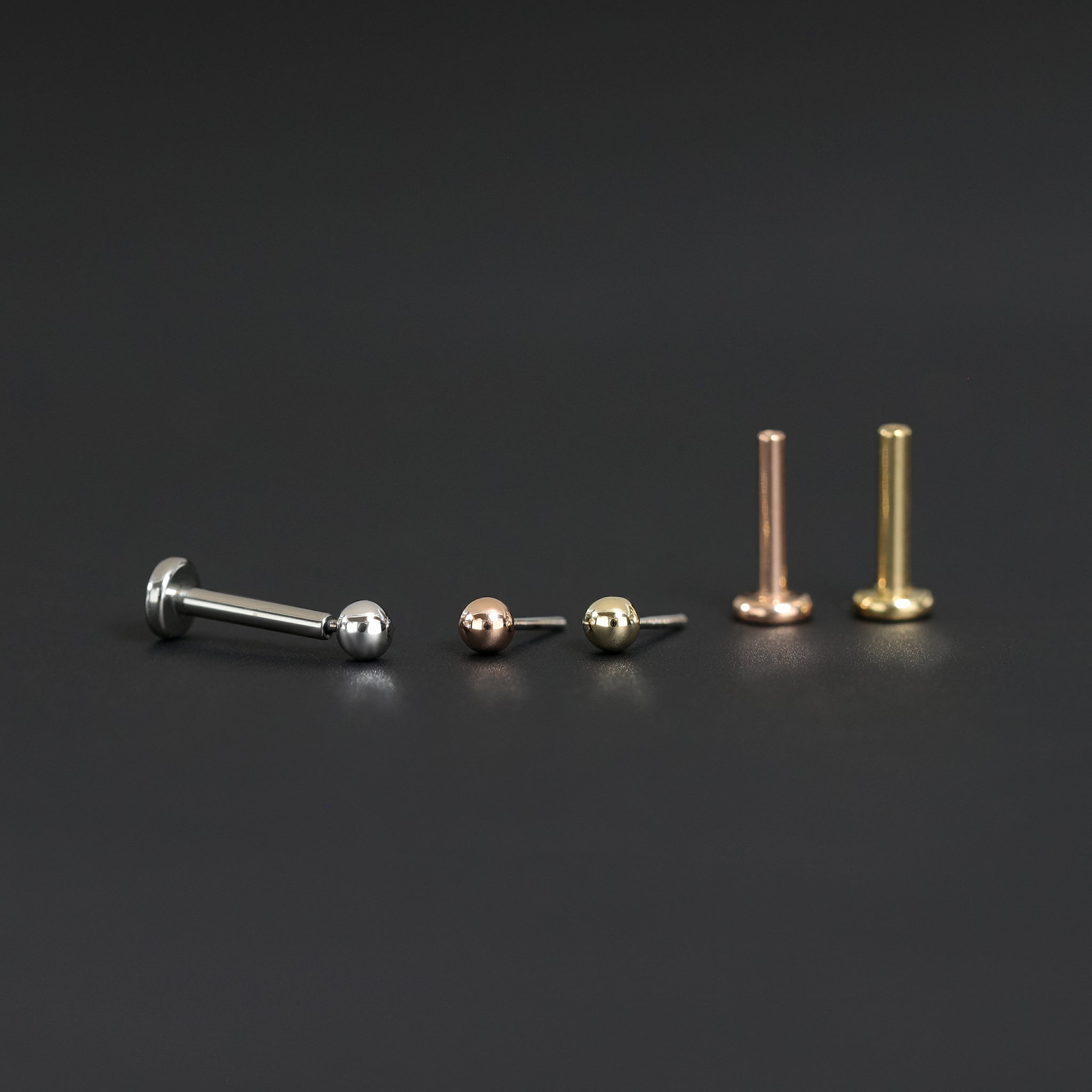 14K Gold Ball studs in yellow gold, white gold and rose gold displayed on black surface in different angles.