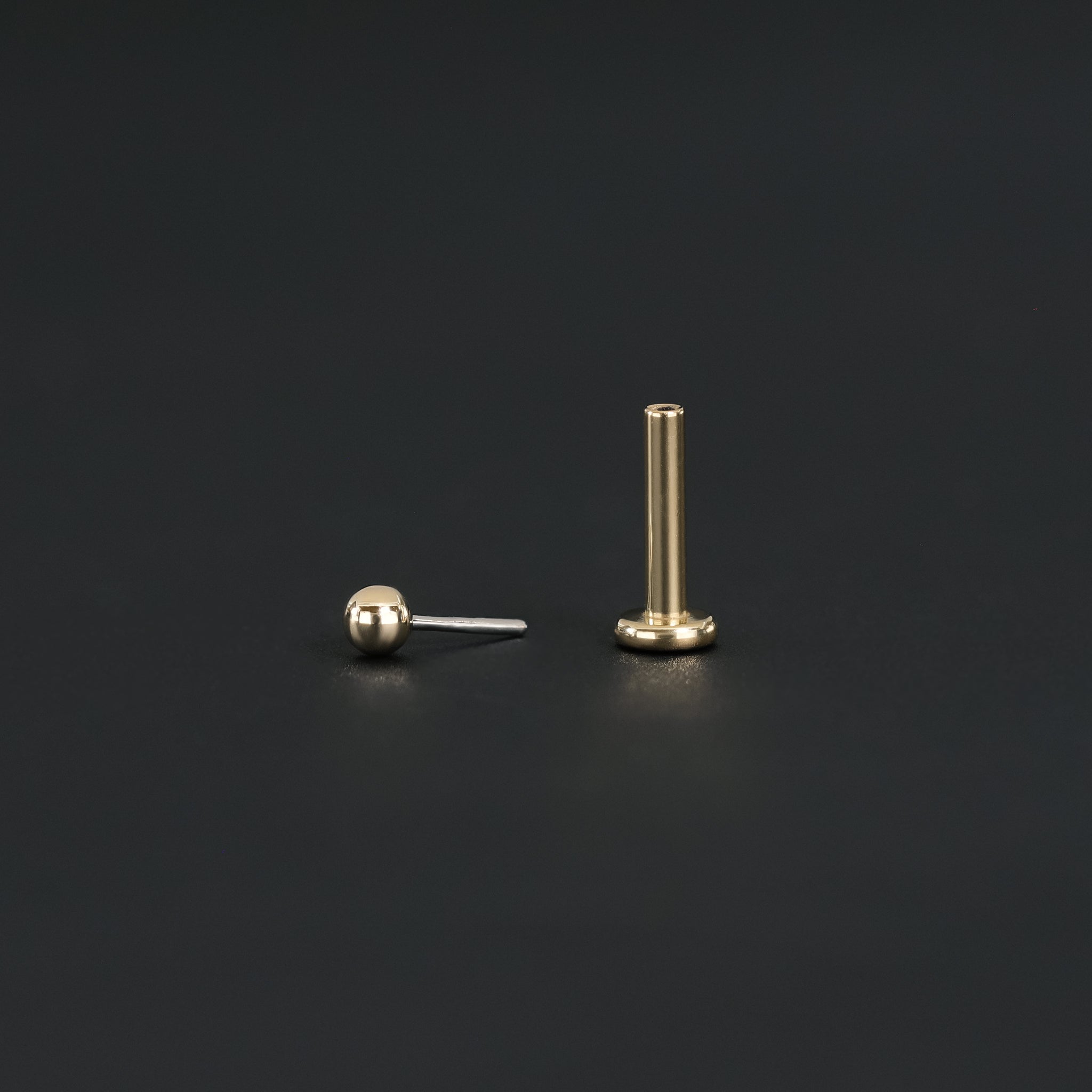 Push pin of 14K Gold Ball studs in yellow gold and Titanium post displayed on black surface.