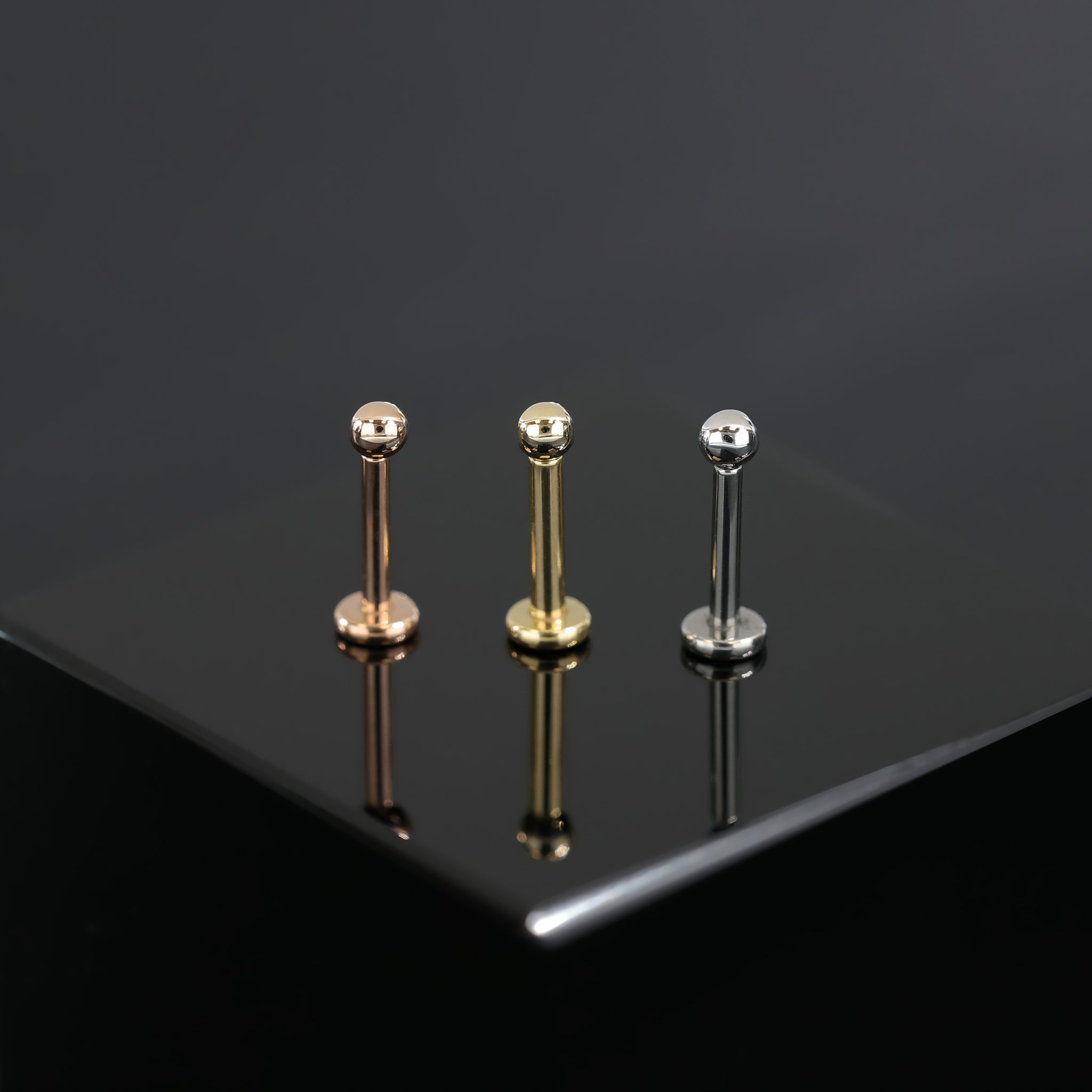 14K Gold Ball studs in yellow gold, white gold and rose gold displayed on black surface.