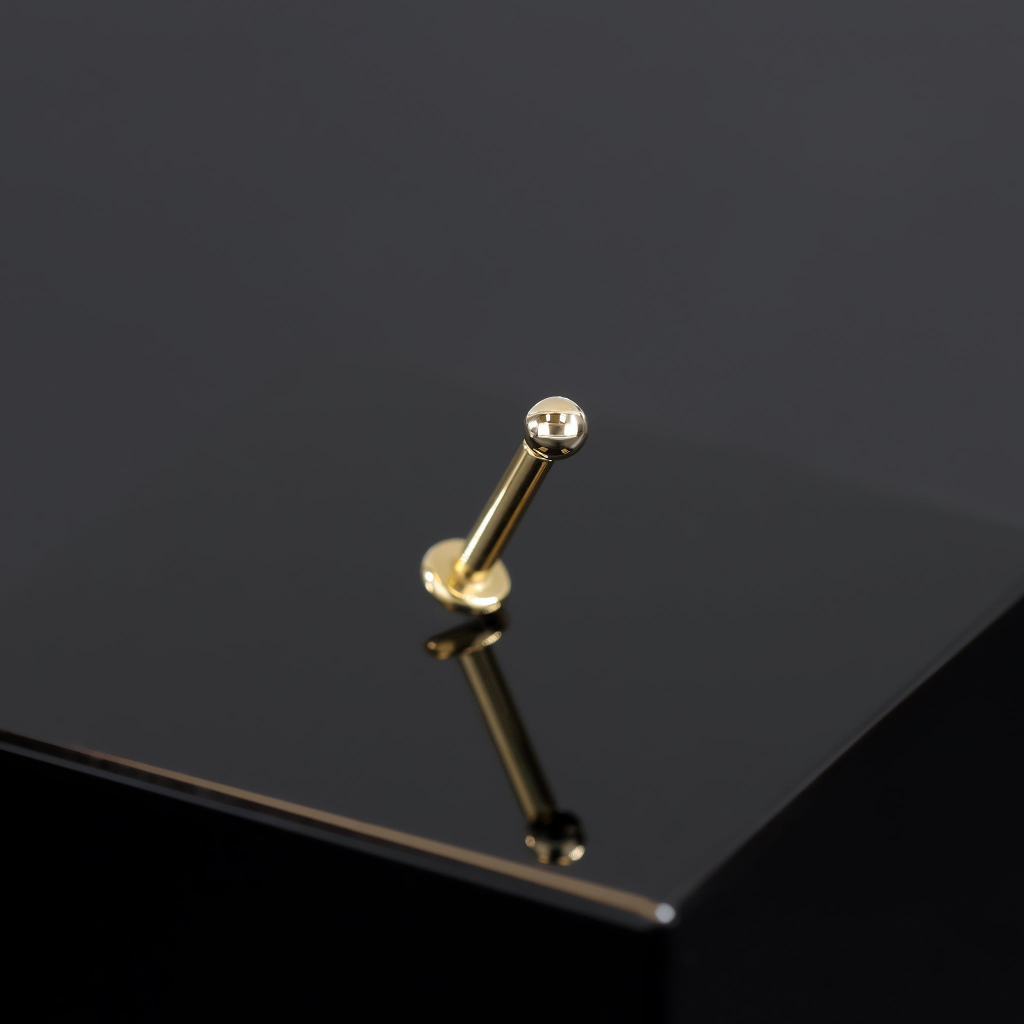 14K Gold Ball studs in yellow gold displayed on black surface in tilted angle.