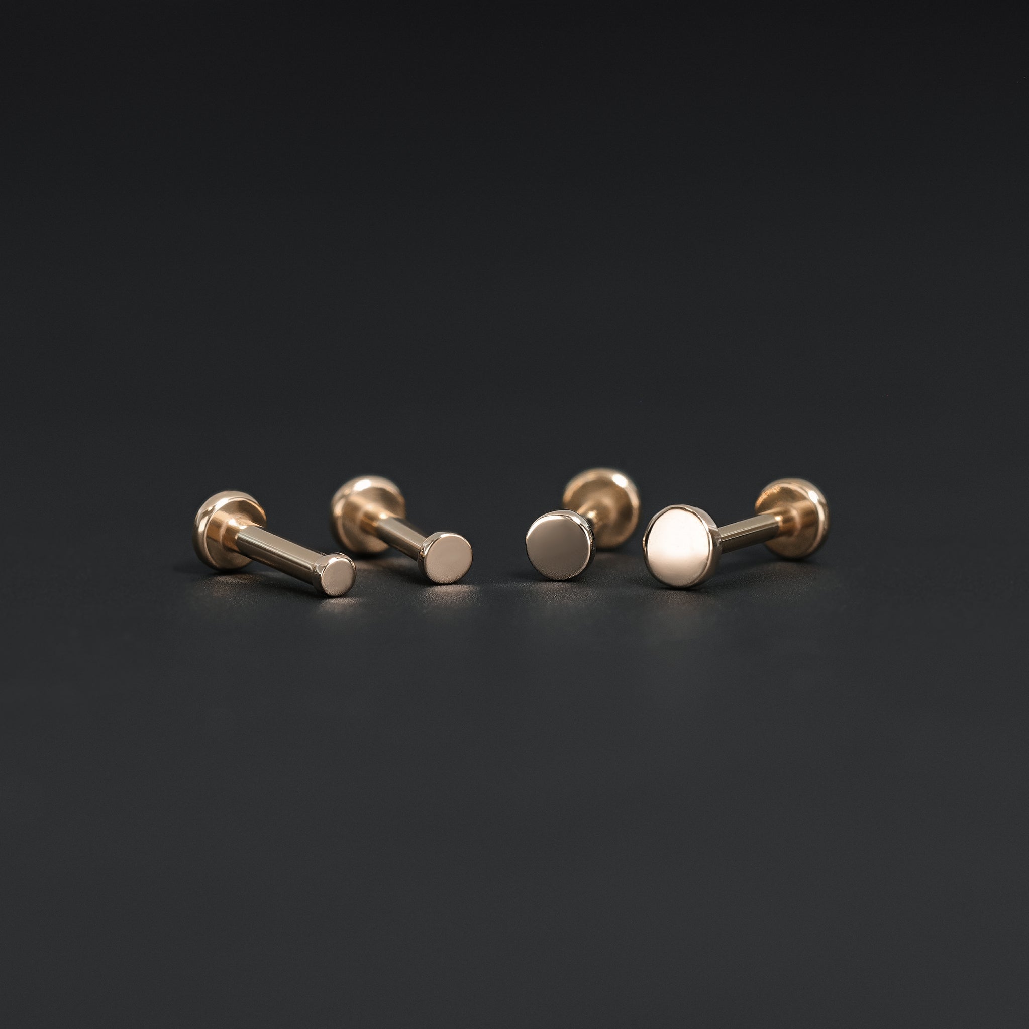 All four sizes 1.5mm, 2mm, 2.5mm and 3mm of 14K gold flat disc studs in rose gold displayed on black surface