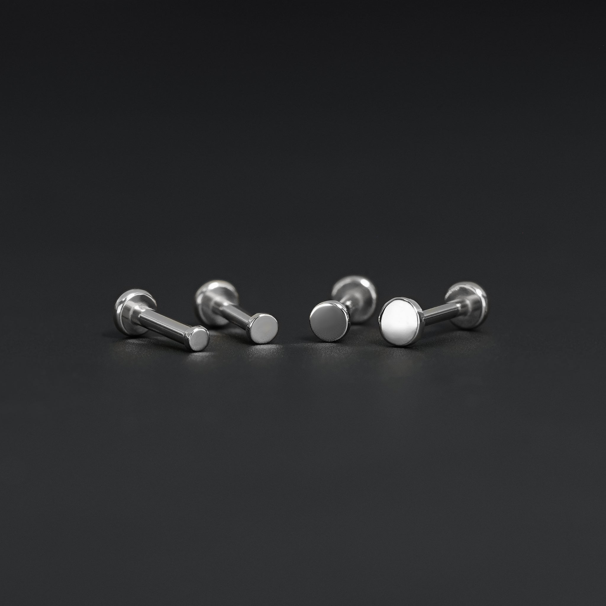 All four sizes 1.5mm, 2mm, 2.5mm and 3mm of 14K gold flat disc studs in white gold displayed on black surface