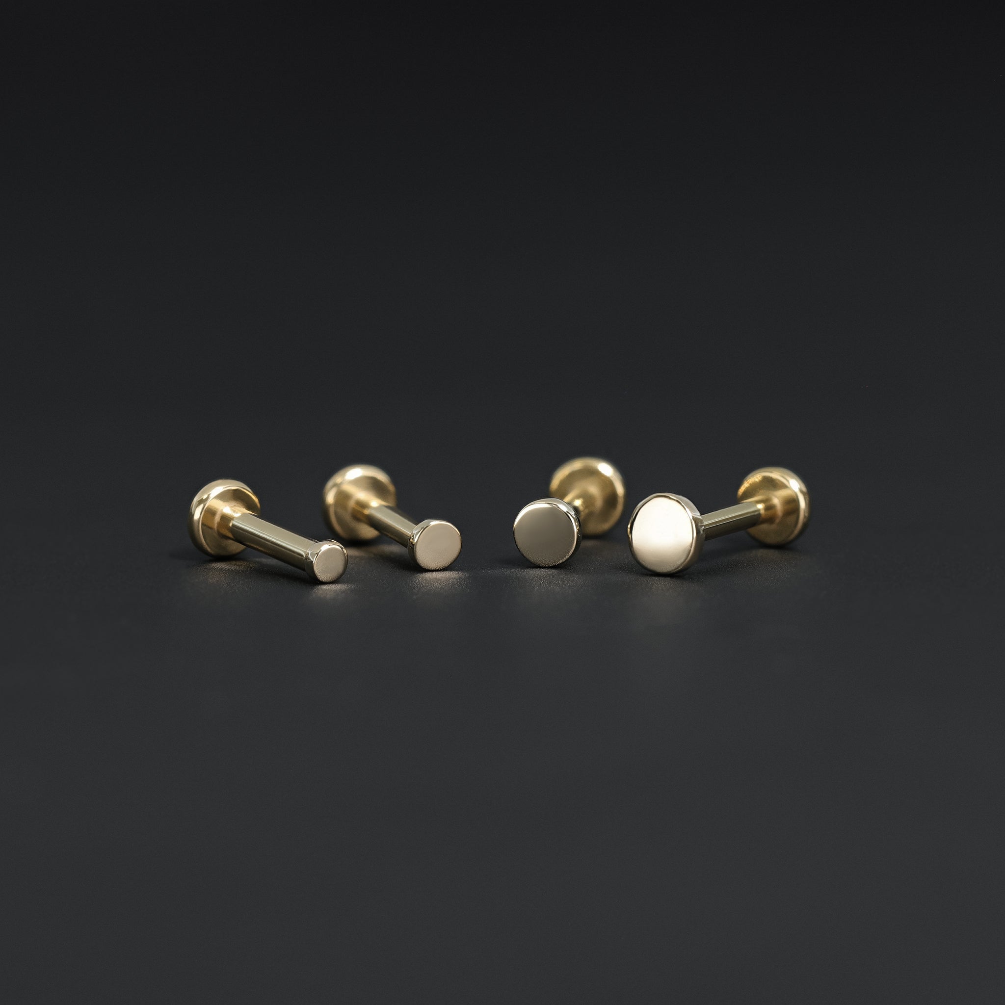 All four sizes 1.5mm, 2mm, 2.5mm and 3mm of 14K gold flat disc studs in yellow gold displayed on black surface