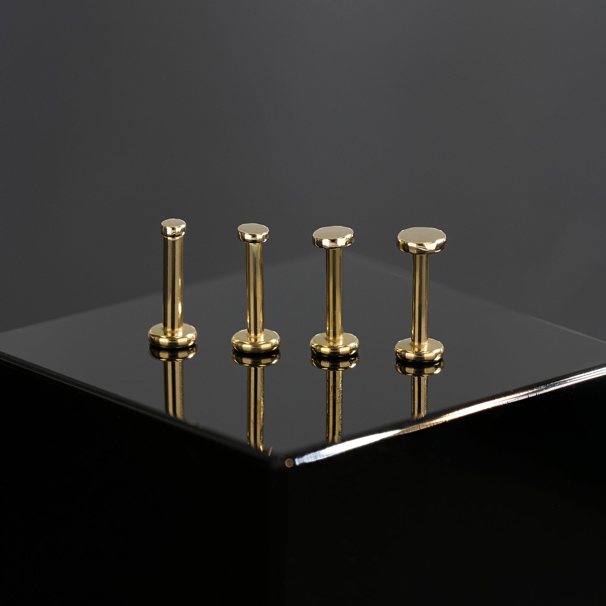 Four sizes of 14K Gold flat disc studs in yellow gold displayed on black surface, featuring their mirror polish finishing.