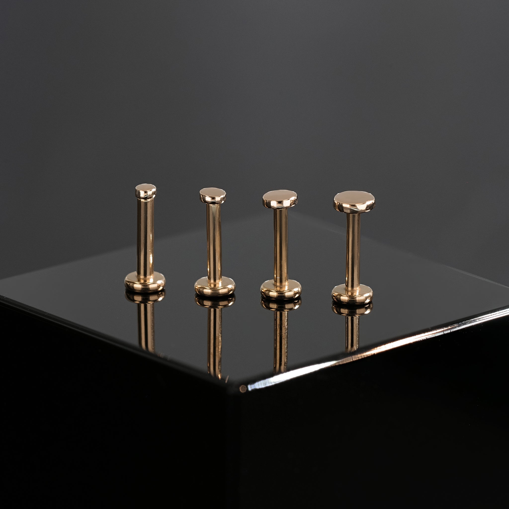 Four sizes of 14K Gold flat disc studs in rose gold displayed on black surface, featuring their mirror polish finishing.