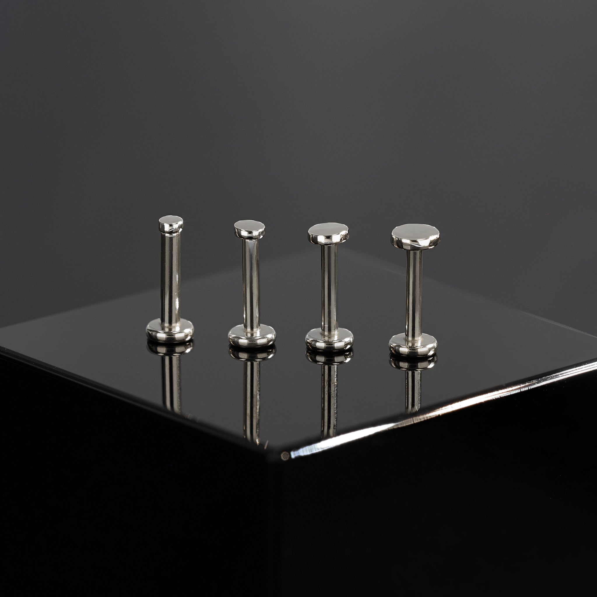 Four sizes of 14K Gold flat disc studs in white gold displayed on black surface, featuring their mirror polish finishing.