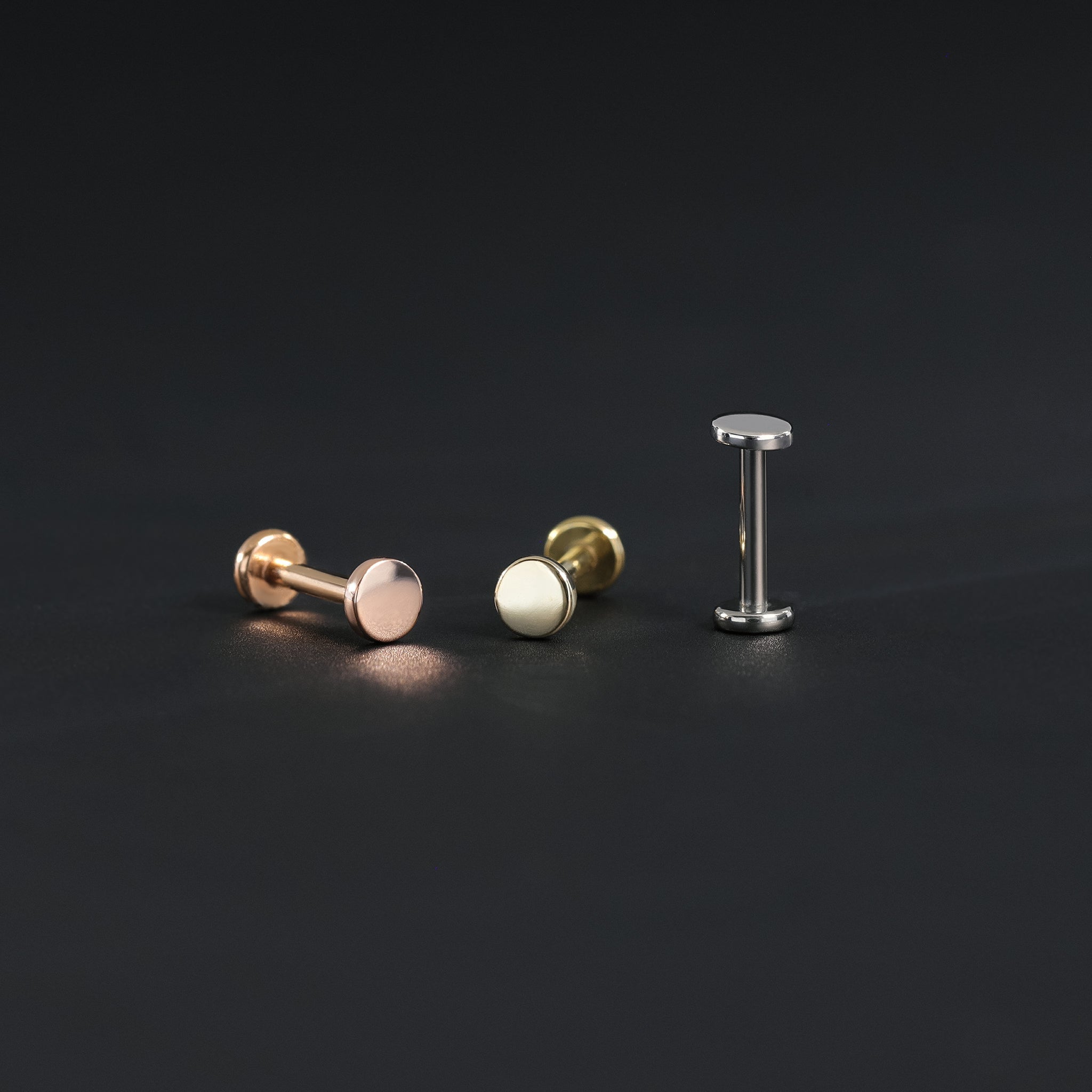 3mm 14K gold flat disc studs in yellow gold, white gold and rose gold displayed in different angles on black surface.