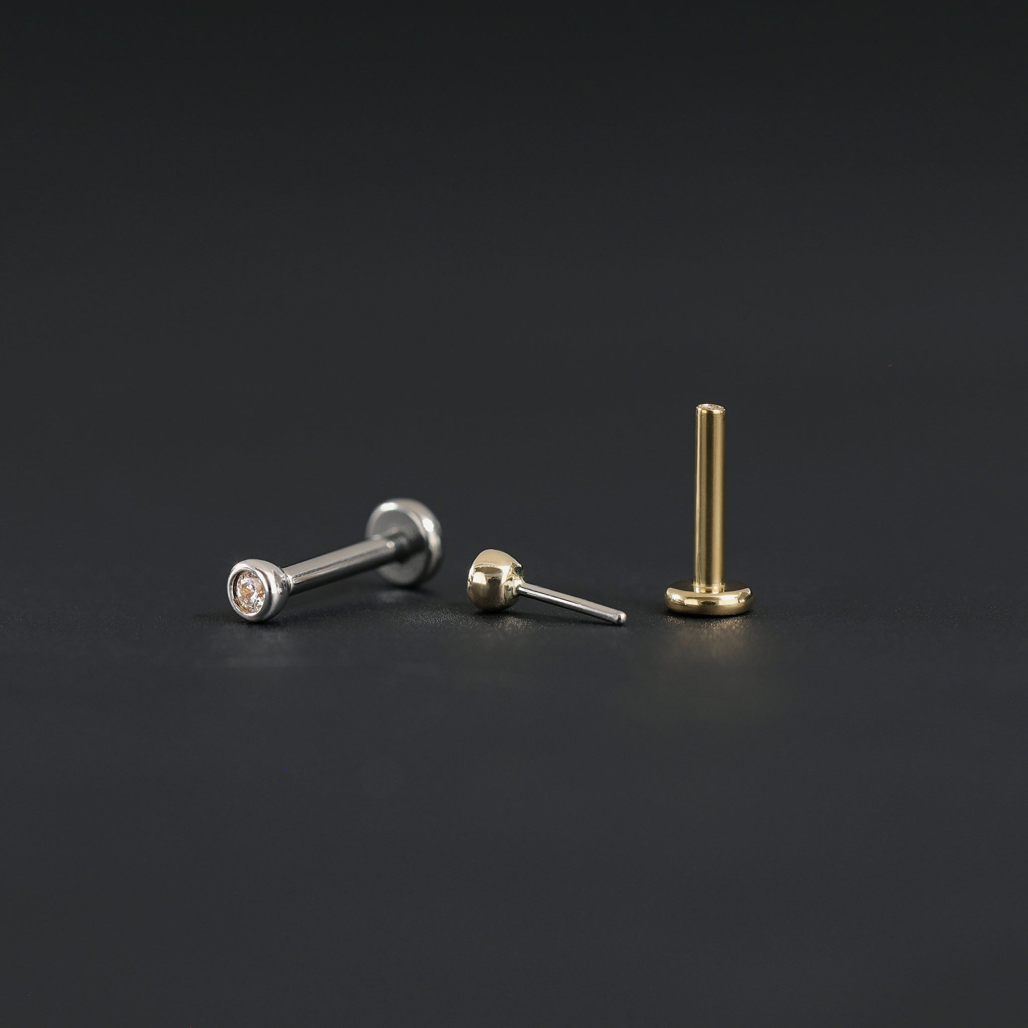 14K Gold Bezel Cubic Zirconia studs in yellow gold and white gold displayed on black surface in different angles.