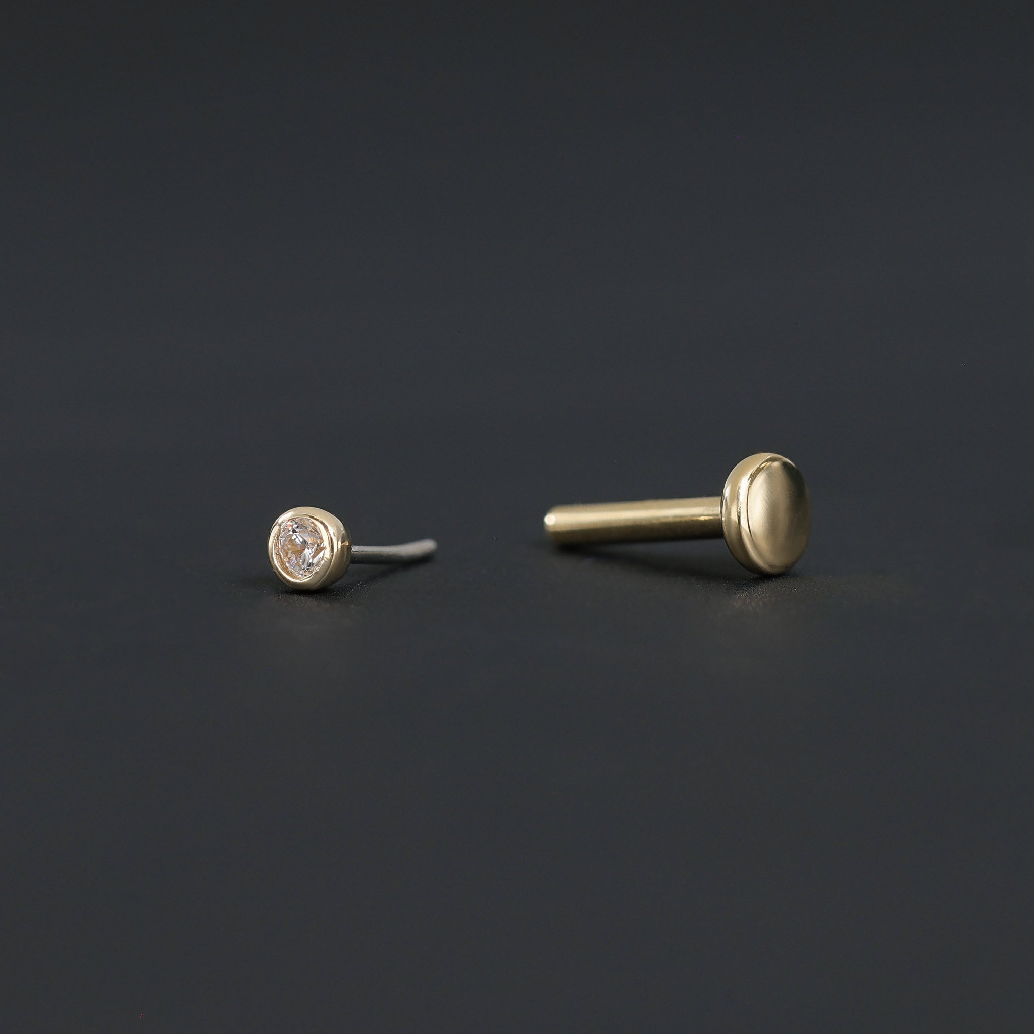 Push pin of 14K Gold Bezel Cubic Zirconia studs in yellow gold and Titanium post displayed on black surface.