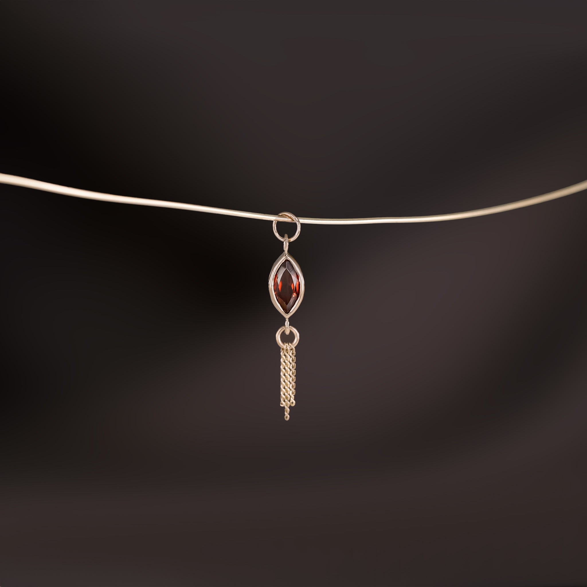 14K gold charm of a a marquise-cut Garnet paired with three delicate gold curb chain tassels