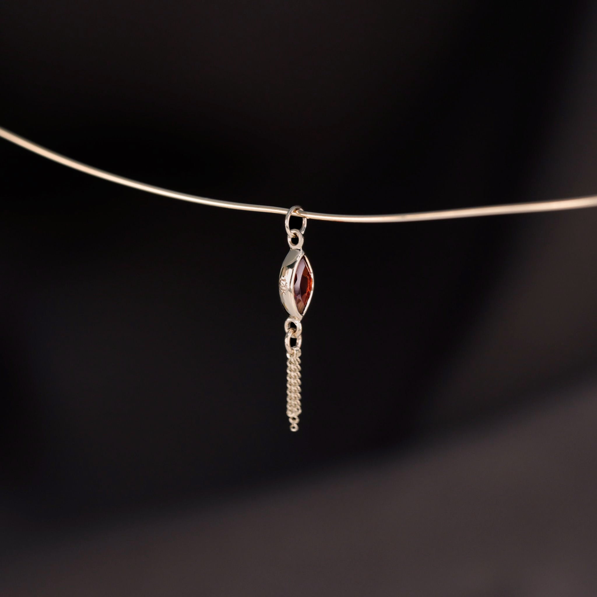 A side view of 14K gold charm of a a marquise-cut Garnet paired with three delicate gold curb chain tassels