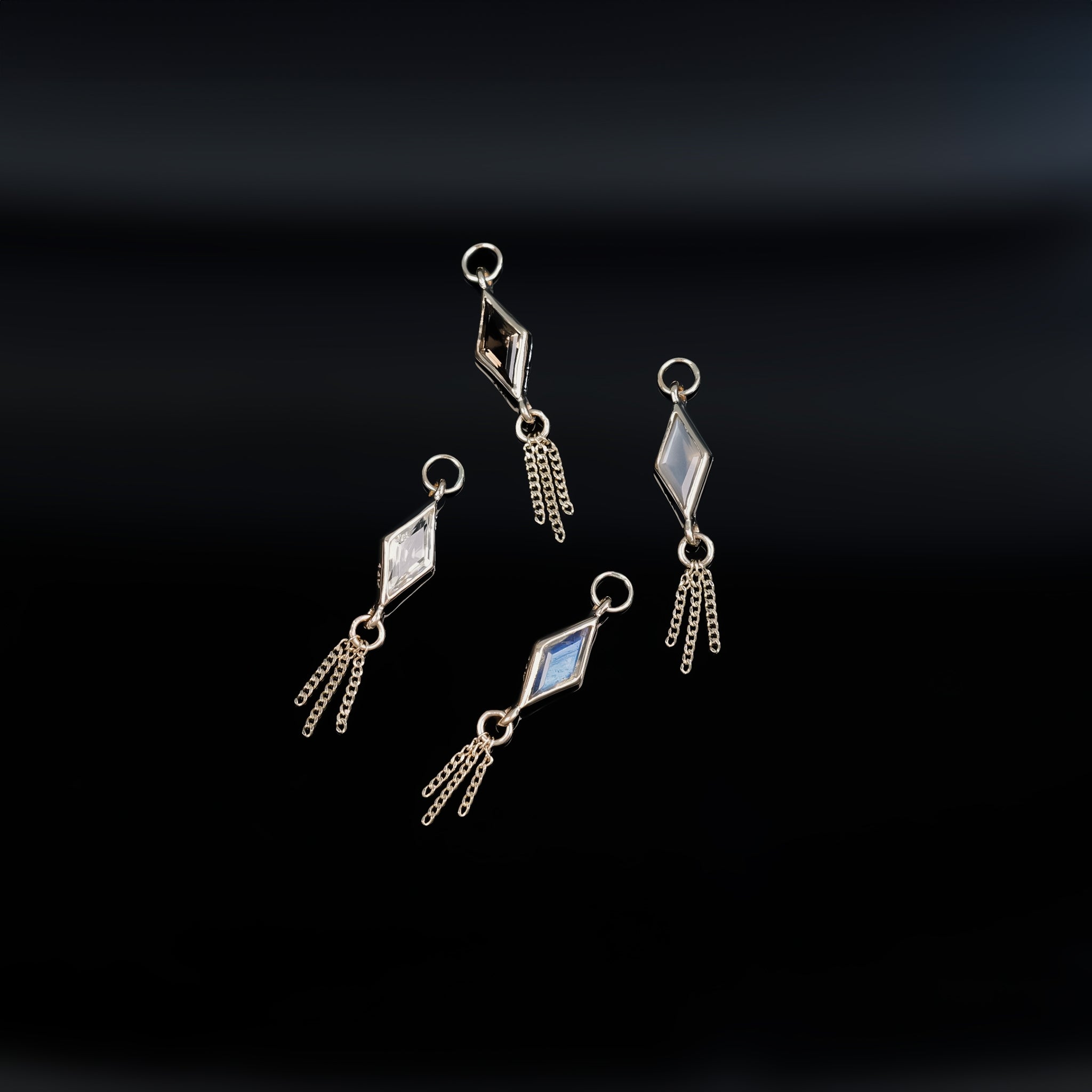 14K gold charm of a kite a Rhombus-cut natural gemstone paired with three delicate gold curb chain tassels laid on black background