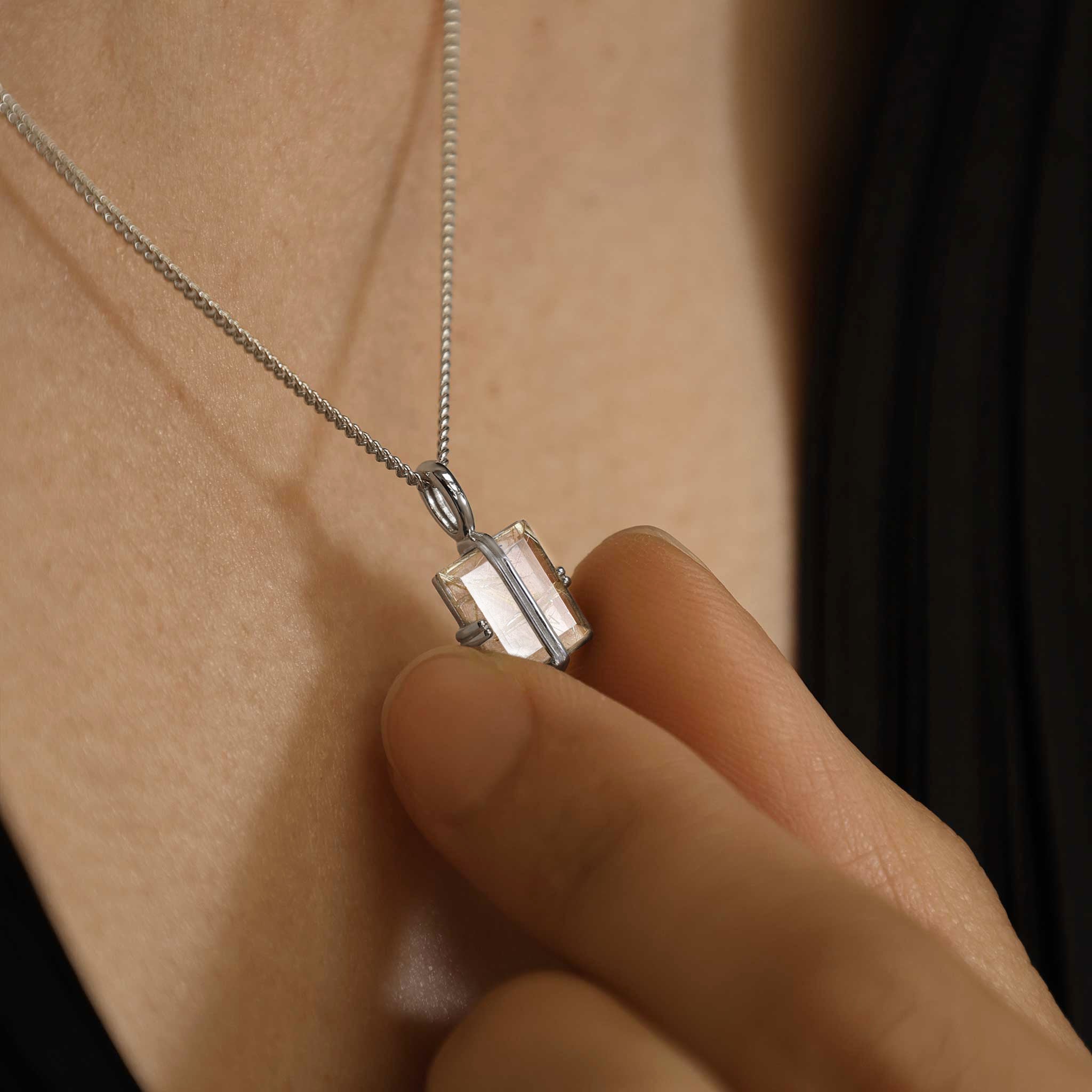Silver necklace with a pendant being held against skin