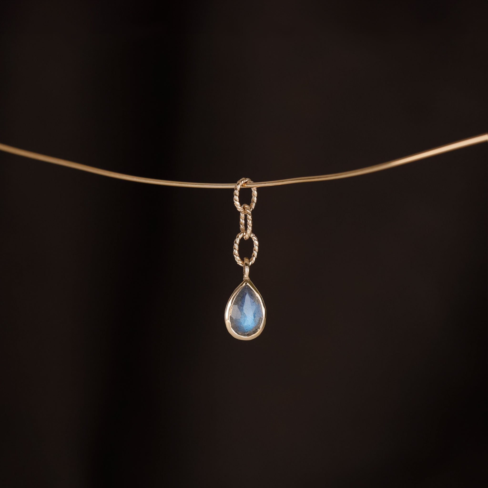 A teardrop shaped charm with Labradorite stone, a gold twisted rope chain design hanging on a golden wire