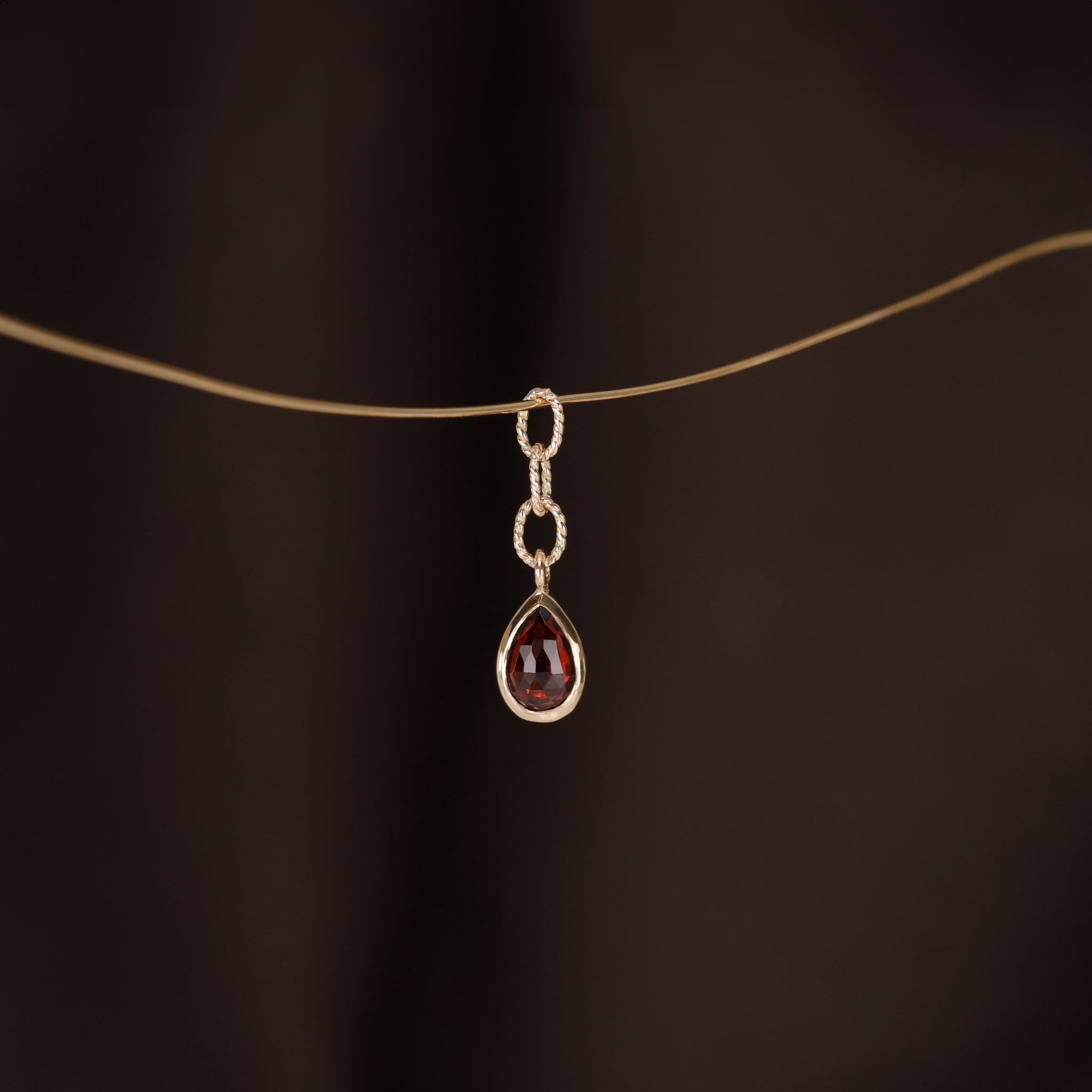 A teardrop shaped charm with Garnet stone, a gold twisted rope chain design hanging on a golden wire