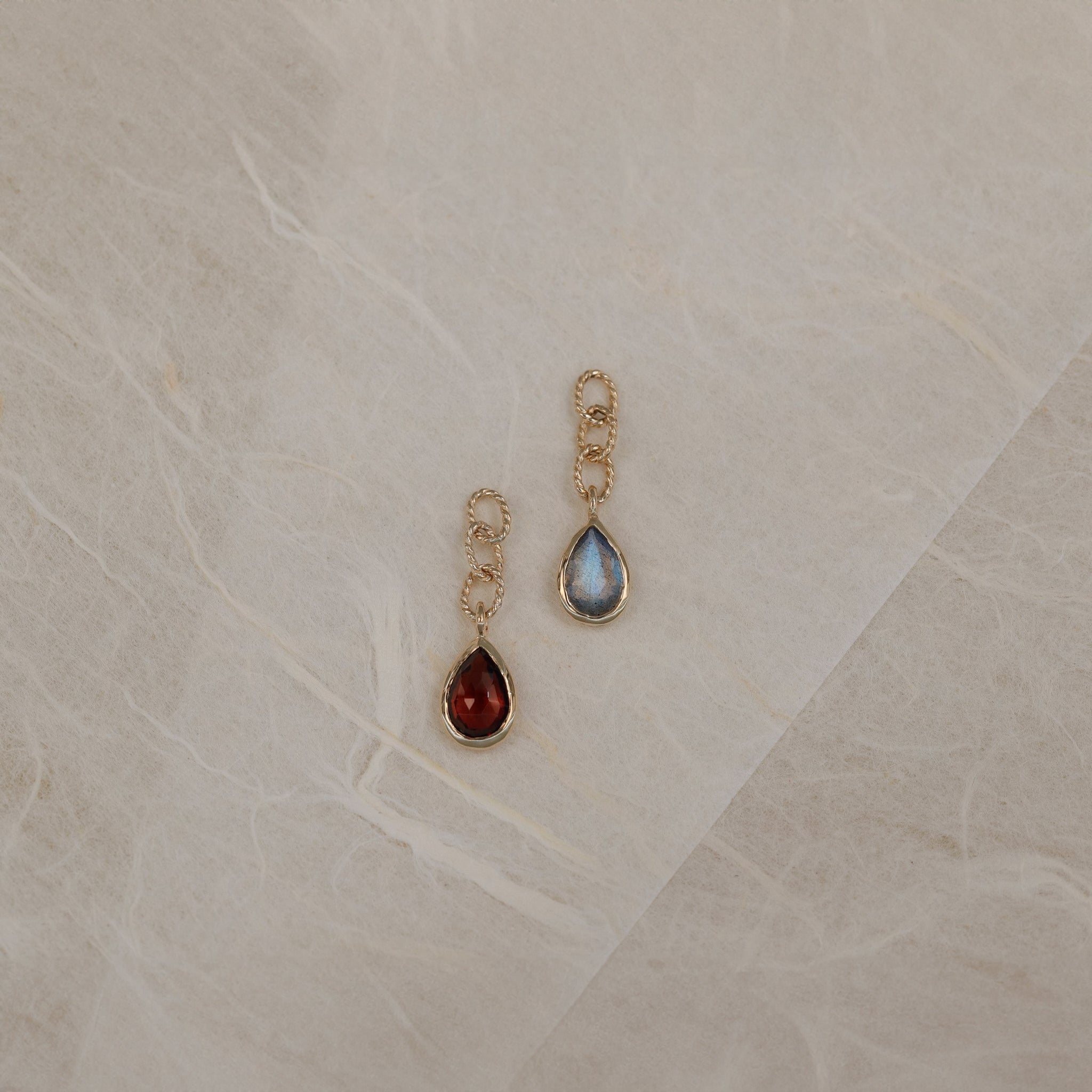 A teardrop shaped charm with Garnet and Labradorite, laid on a white paper