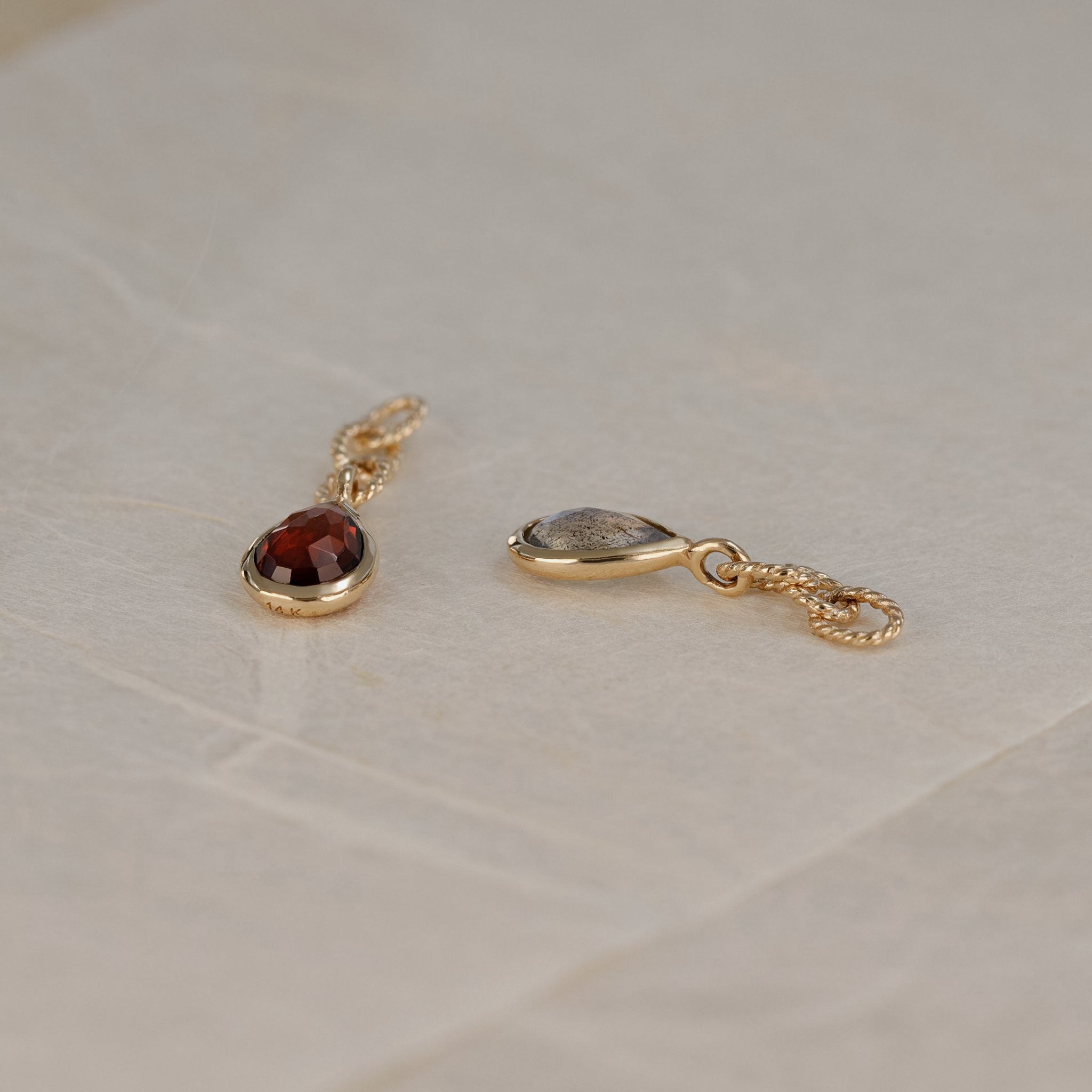 A detail side view of a teardrop shaped charm with Garnet and Labradorite, laid on a white paper