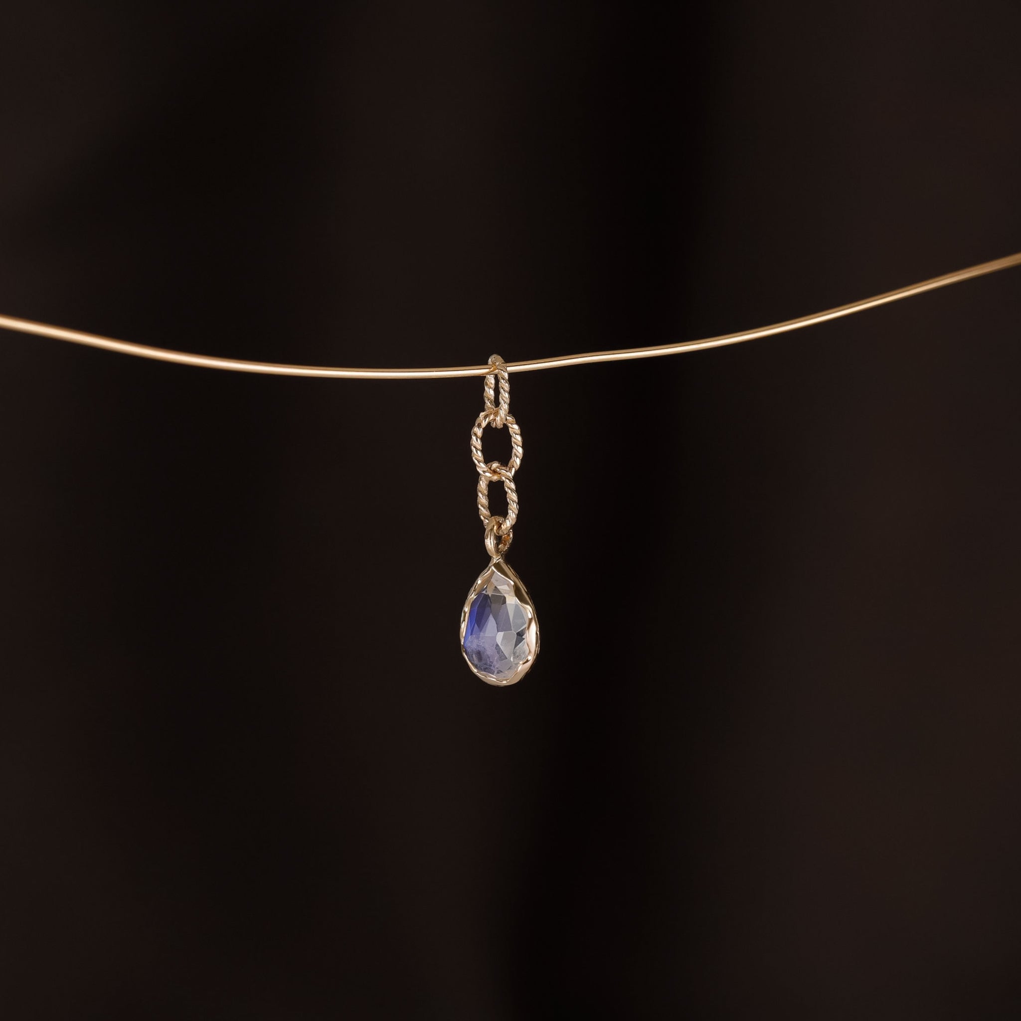 Charm of a teardrop Rainbow Moonstone with gold twisted rope chain hanging on a golden wire