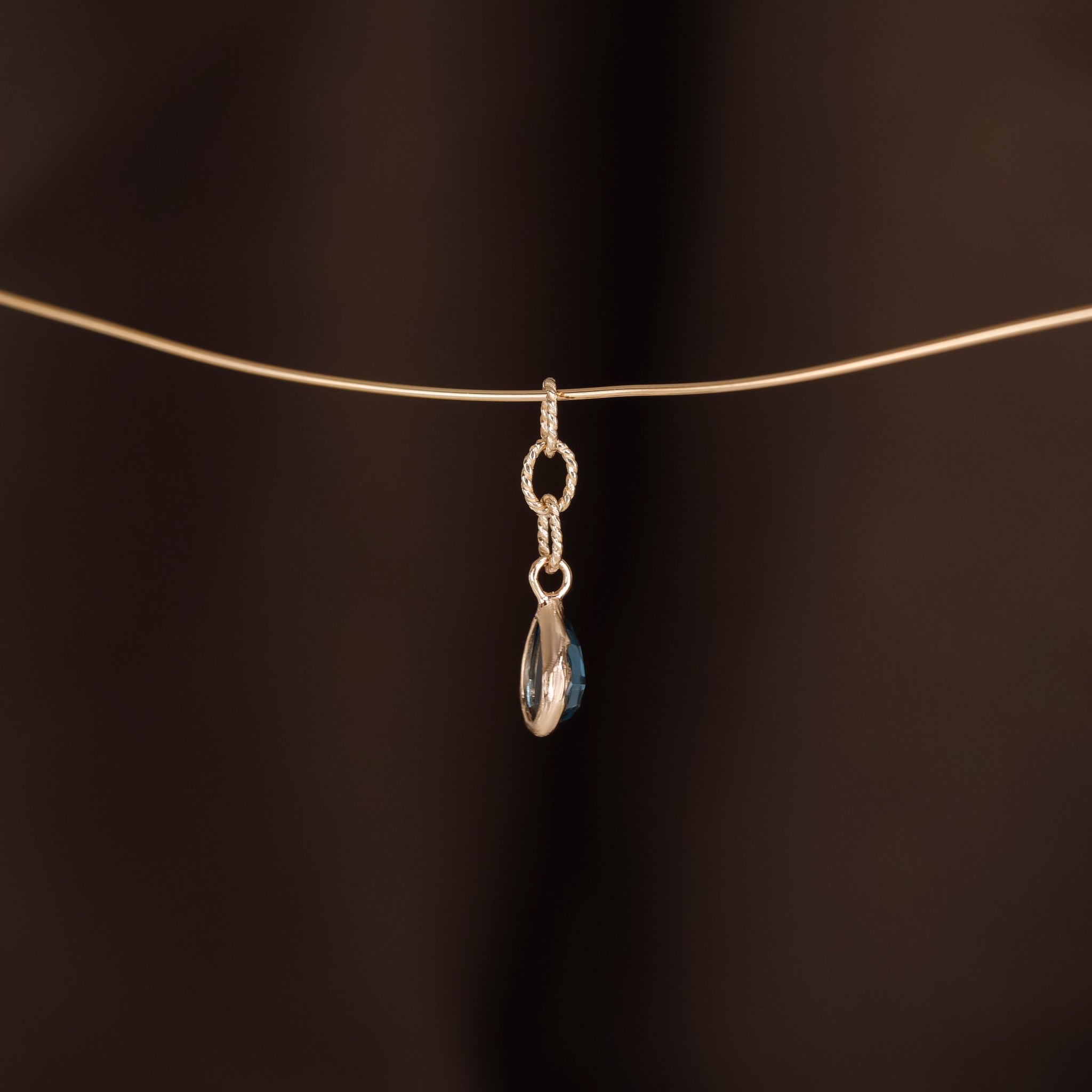 Charm of a teardrop London Blue Topaz with gold twisted rope chain hanging on a golden wire