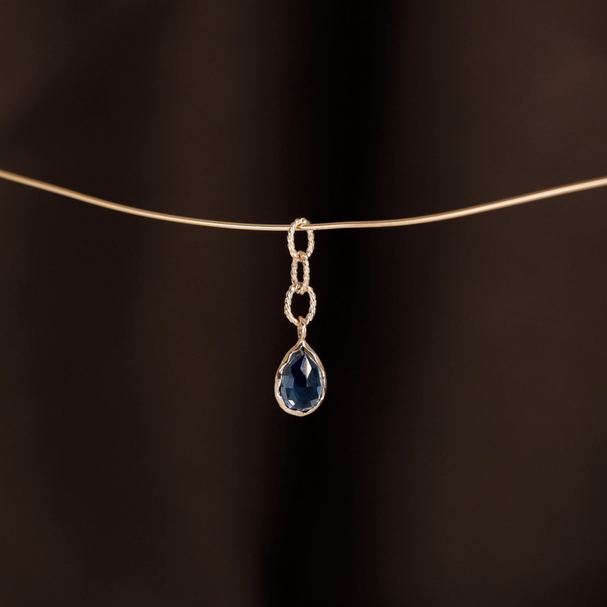 Charm of a teardrop London Blue Topaz with gold twisted rope chain hanging on a golden wire