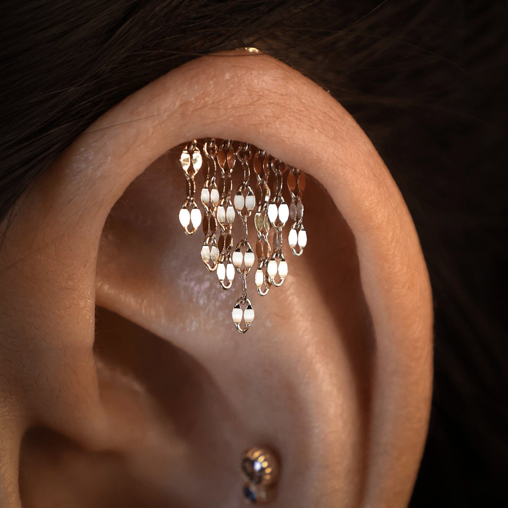 Close-up of an ear with a gold earring featuring dangling beads.