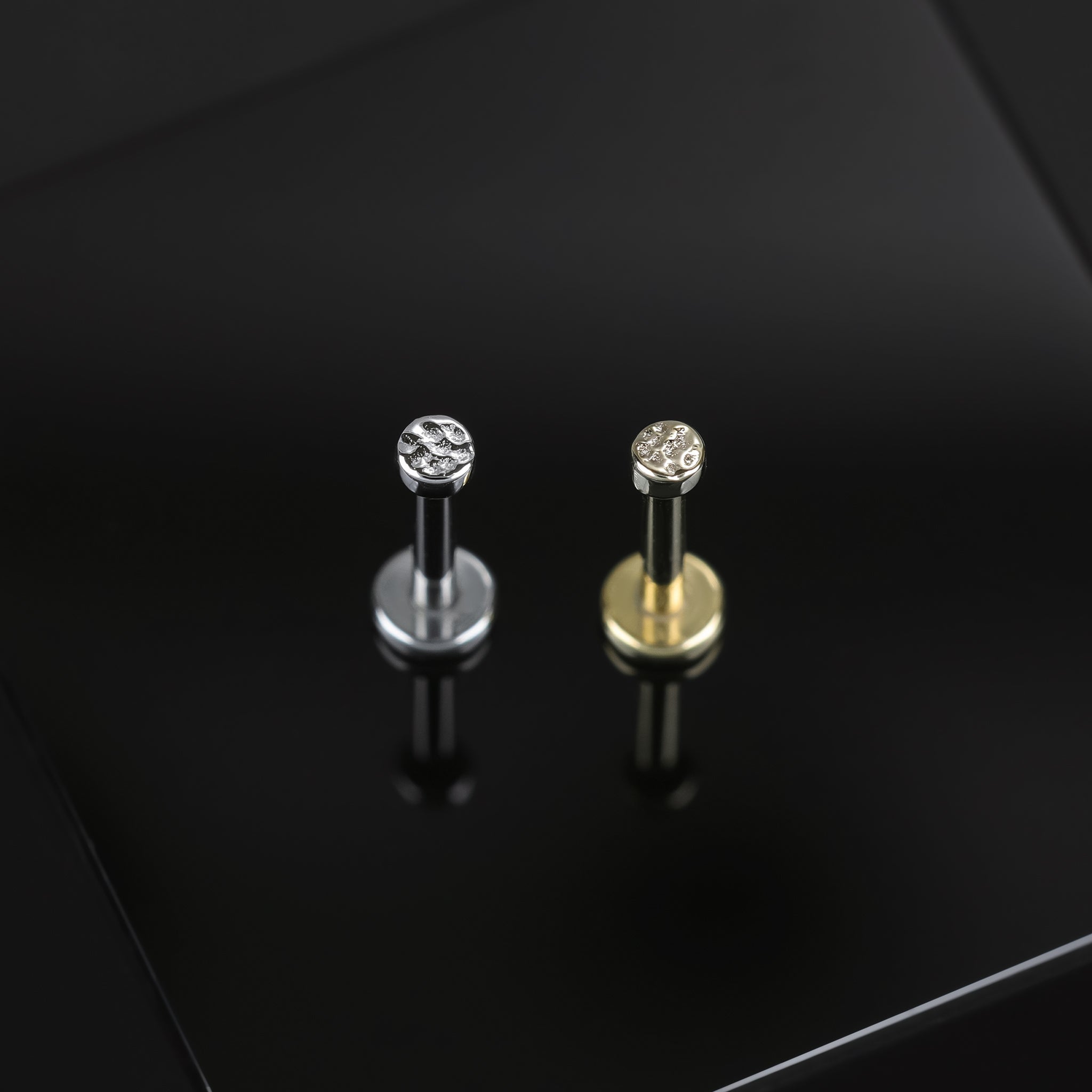 2mm 14K Gold Hammered disc studs in yellow gold and white gold displayed on black surface, featuring its textured surface on a disc.