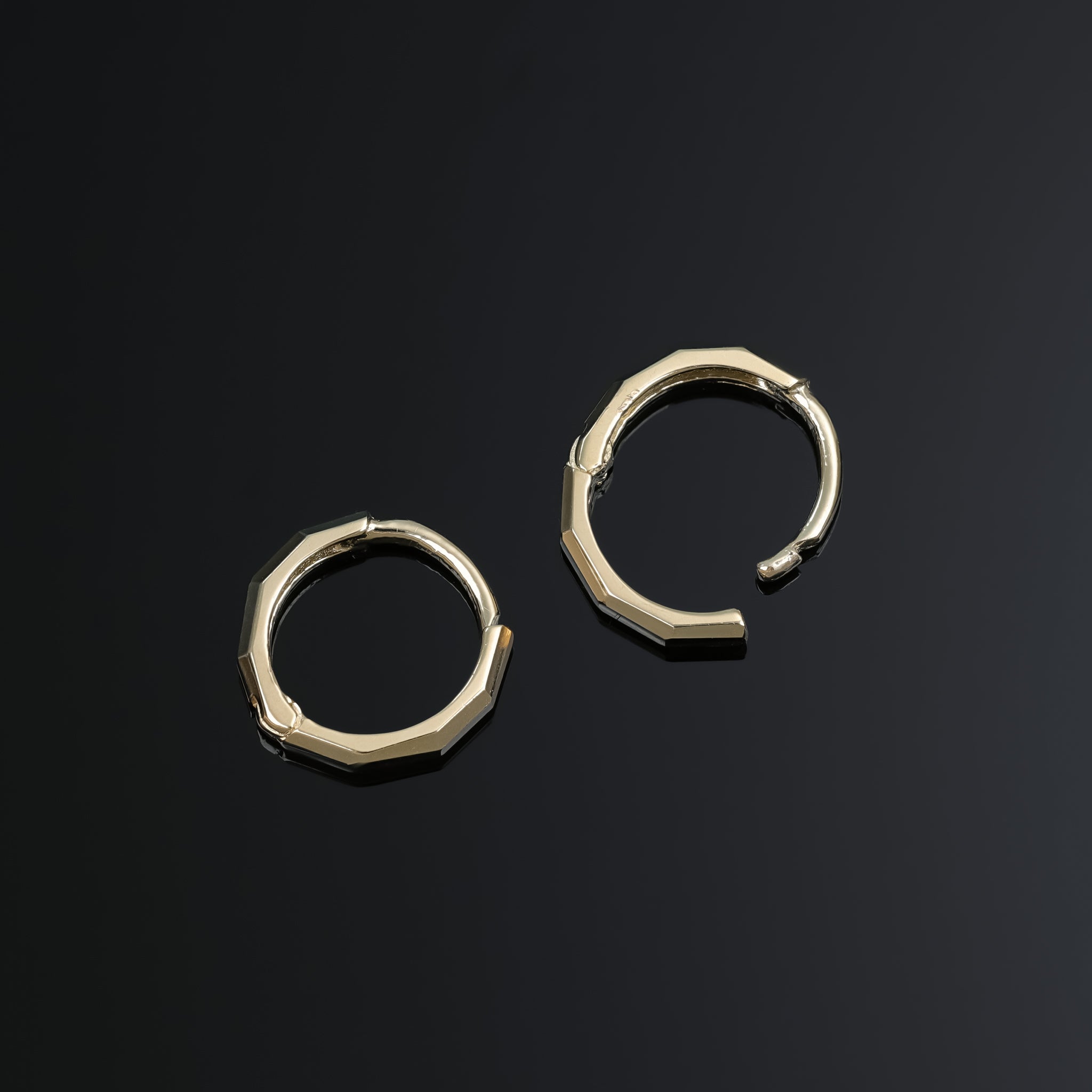 A brilliant faceted diamond-cut design Huggie Hoop in 7mm displayed on a dark surface one standing upright and the other opened