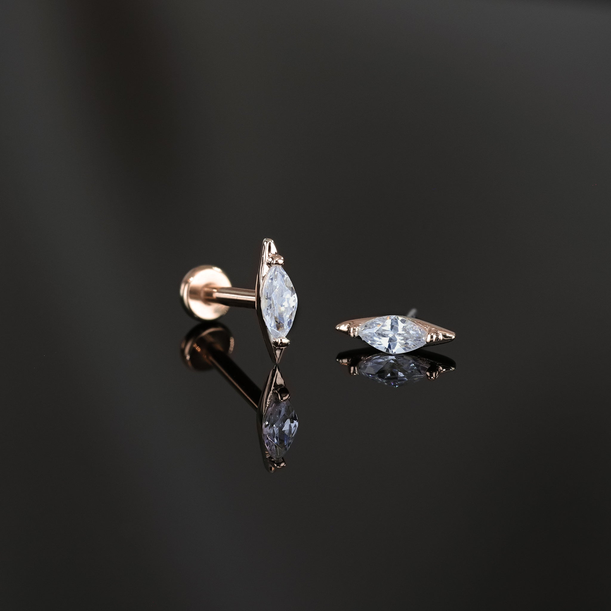 Two marquise-shaped cubic zirconia studs in 14K rose gold displayed on a dark surface, one standing upright to showcase its sleek profile and the other laid flat to highlight the sparkling facet-cut stone.