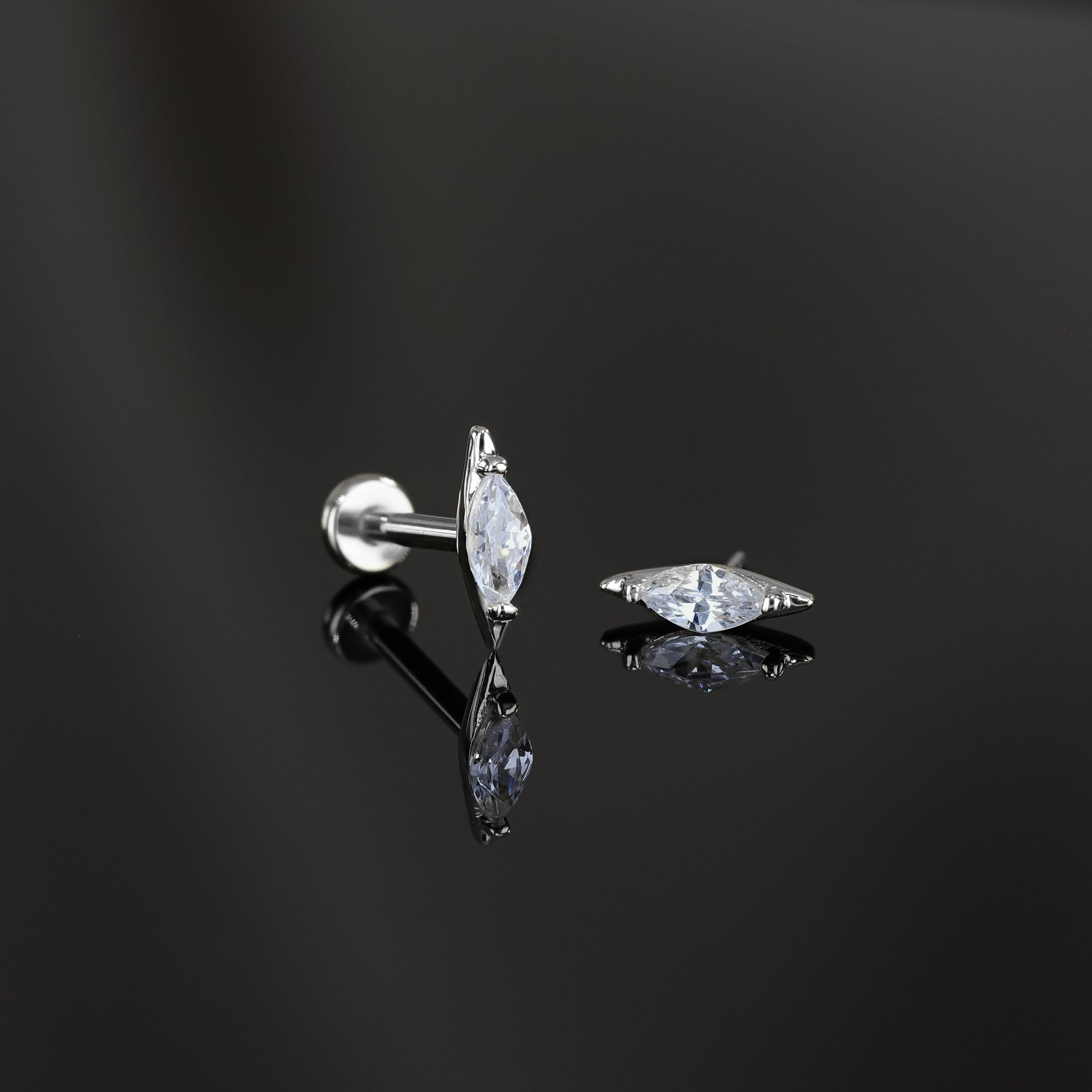 Two marquise-shaped cubic zirconia studs in 14K white gold displayed on a dark surface, one standing upright to showcase its sleek profile and the other laid flat to highlight the sparkling facet-cut stone.