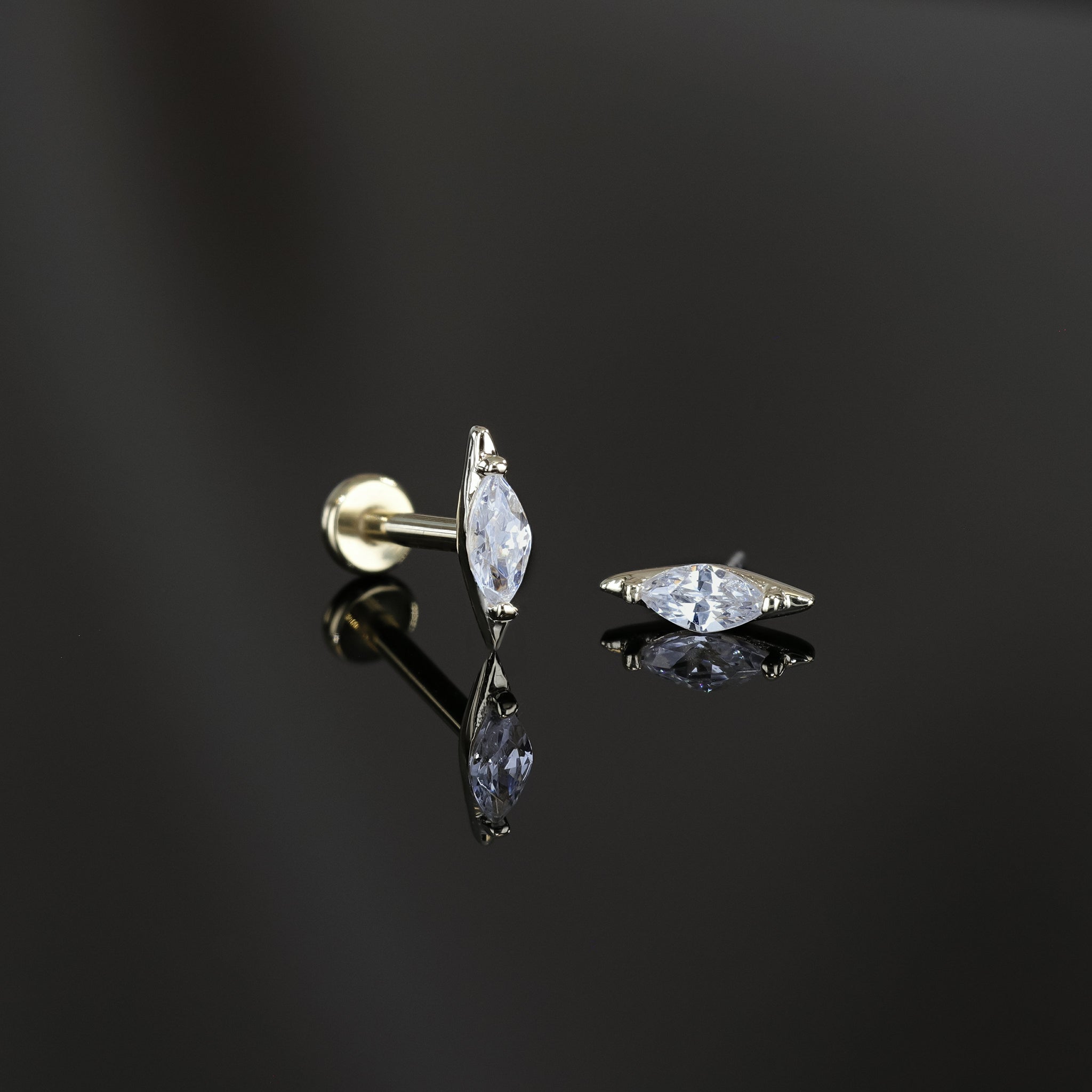 Two marquise-shaped cubic zirconia studs in 14K yellow gold displayed on a dark surface, one standing upright to showcase its sleek profile and the other laid flat to highlight the sparkling facet-cut stone.